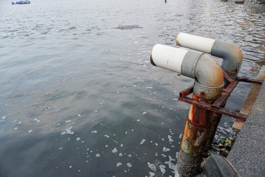 Industrial pipes discharging water into the sea with foam.