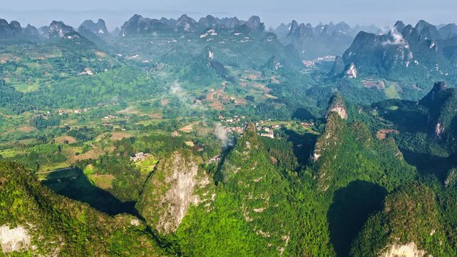 Aerial view of green karst mountain peaks and lush valleys near Guilin, Guangxi, China, illuminated by bright natural sunlight under a blue sky.