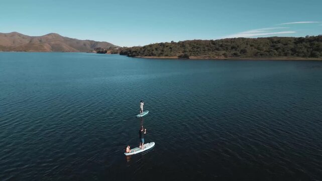 Aerial view of two paddleboarders gliding across a still reservoir