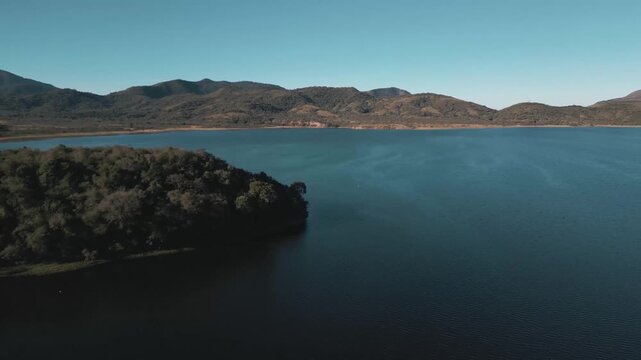 Aerial drift along a shadowed reservoir inlet beneath rolling highlands