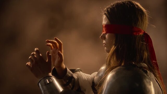 Blindfolded Caucasian young woman in knight armor reaching hands forward, exploring space. Footage suitable for fantasy films, game trailers, cinematic themes of blind trust or uncertainty