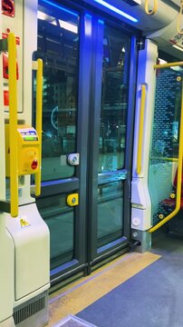 Inside a modern tram interior with closed automatic glass doors in Warsaw, Poland, showing blue LED illumination and yellow handrails for urban public transport.