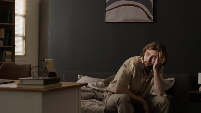 Tired young adult Caucasian man waking up, stretching arms, rubbing face, then standing up. Useful for sleep health awareness, fatigue, burnout, wellness advertising