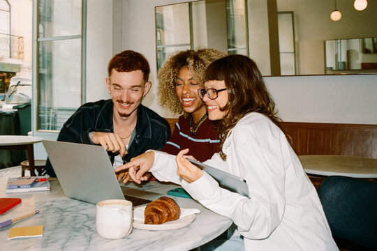 Gen Z business team collaborating over laptop in cafe