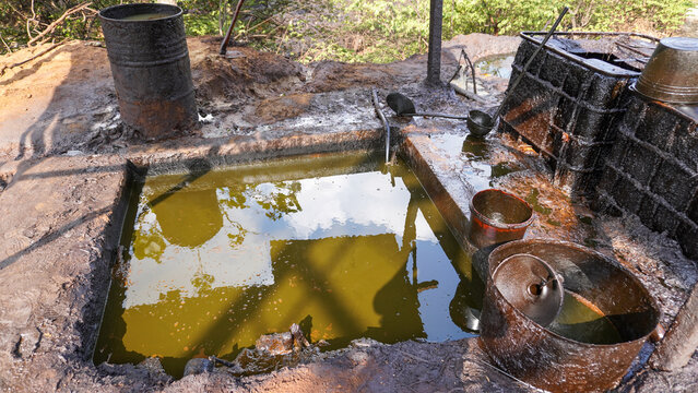 Crude oil reservoir pool and storage tanks at a traditional petroleum mining site in Wonocolo, Bojonegoro, Indonesia. Rural industrial energy extraction, fuel production, and crude processing site.