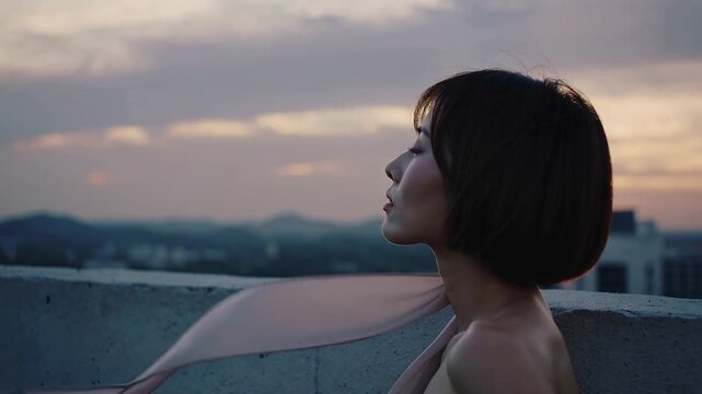 Reacting to sunset breeze Asian woman tilting chin on rooftop parapet watching scarf arc