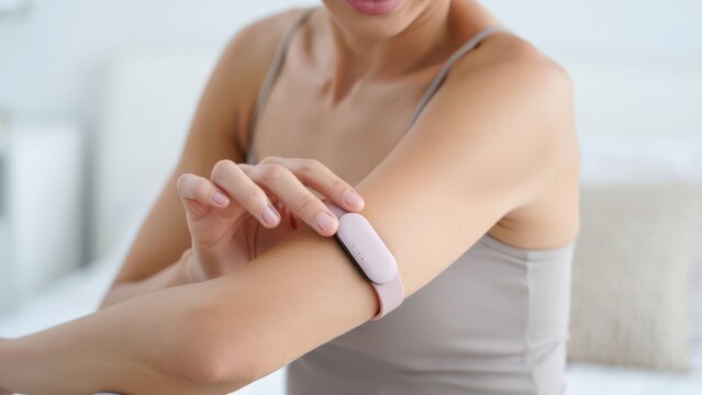 Woman adjusting pink smart fertility band on upper arm, wearable ovulation sensor for hormone tracking, compact femtech device for daily monitoring