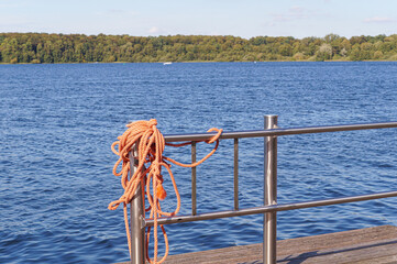 Orange mooring rope tied to a metal railing on a lakeside dock © SCHWERIN BY WATER