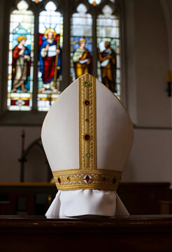 Religion and faith, bishop mitre hat on a church pew with stained glass windows in the background for Christian liturgy and ecclesiastical tradition