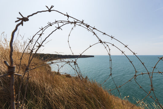 Grassy cliffs overlook the English Channel with barbed wire in the foreground in the Normandy region of France.