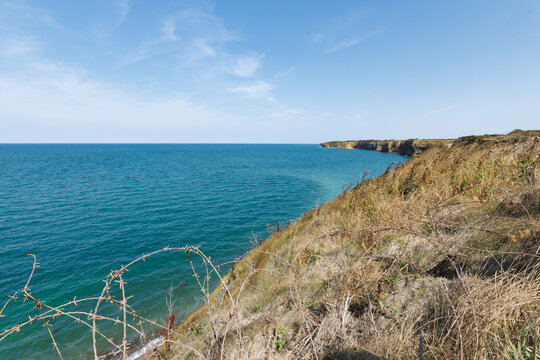 Grassy cliffs overlook the English Channel with barbed wire in the foreground in the Normandy region of France.