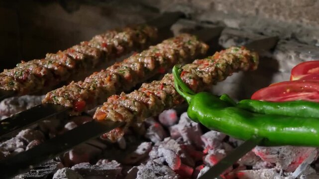 Traditional Adana Kebab with peppers and tomatoes cooking on a charcoal barbecue