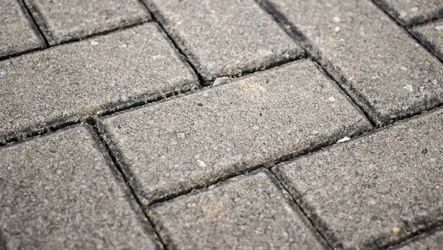 Close-up of textured gray rectangular paving stones arranged in a staggered pattern, showing weathered surfaces, dark joints, and subtle geometric details.