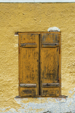 Close up of yellow plastered wall with weathered brown wooden window shutters, rustic texture and traditional vernacular architecture detail on old cottage