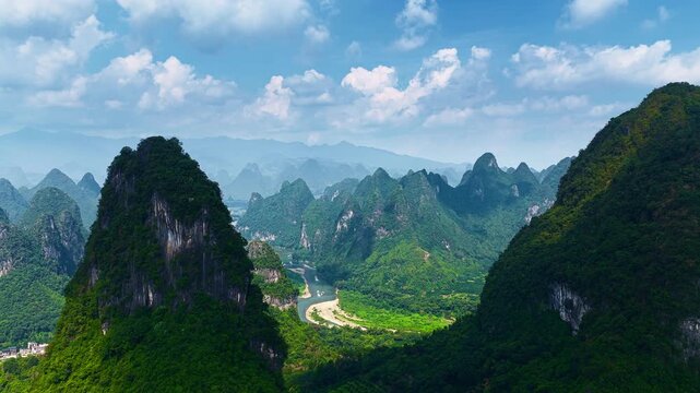 Aerial view of lush green karst mountain peaks and a winding river under a blue sky with clouds in Guilin, China during daytime.