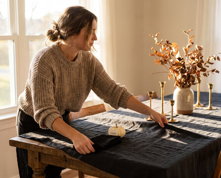 Woman setting black linen tablecloth with brass candlesticks for halloween dinner party