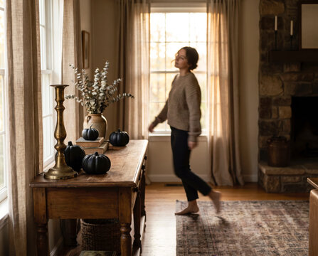 Woman walking toward bright window past console table styled with black halloween pumpkins