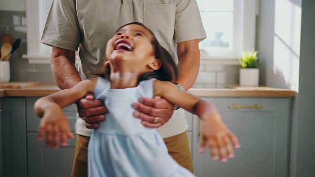 Spinning child in blue dress as adult grabbing torso and pivoting for play in kitchen, wristwatch