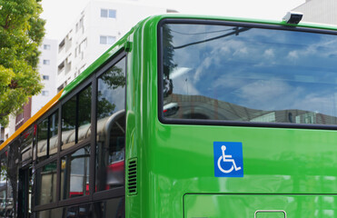 Rear view close up of green public bus with international wheelchair accessibility symbol. Accessible public transport, urban city bus, universal design, and eco friendly commuting concept. © Pat