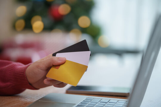 Woman holding three credit cards beside a laptop during Christmas, representing online shopping, holiday spending, digital payment, e-commerce checkout, seasonal sales and retail discounts.