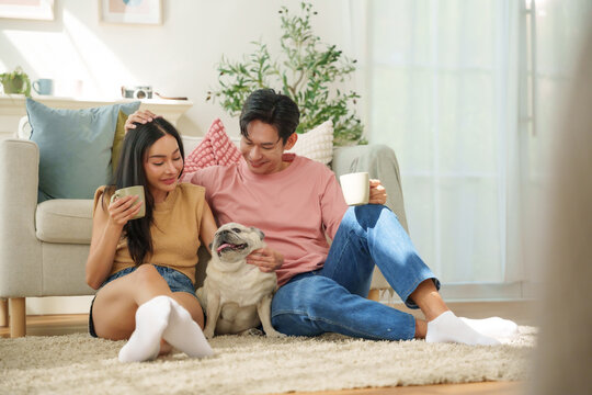 Happy Asian couple relaxing with their pug on the living room floor, representing pet companionship, love, bonding, relationship and cozy home lifestyle.