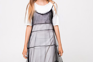 Girl wearing a black dress with sheer layers stands against a plain background during a studio photoshoot. She has long hair and appears to be looking at the camera. background is plain and bright. © SValeriia