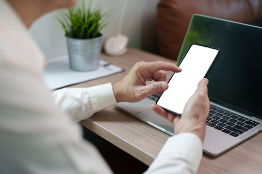 Man using a smartphone beside a laptop while working at home, representing multitasking, online browsing, mobile communication.
