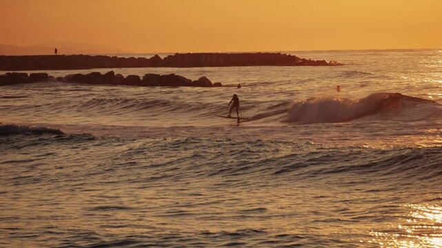 Silhouette of surfers in the sea at sunset, surfing waves against golden sky