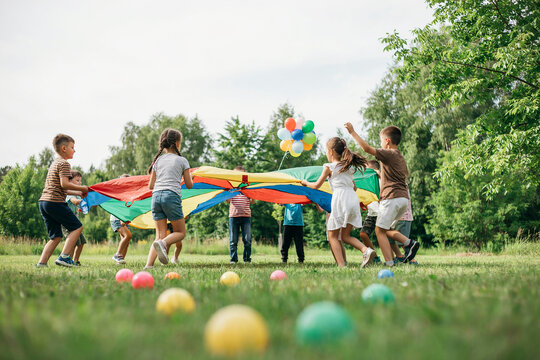 Group of diverse children playing with a colorful parachute and balloons in a park