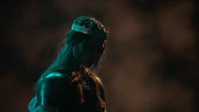 Young Caucasian woman in knight armor wearing crown looking up and backwards with wind blowing hair. Footage ideal for fantasy video game marketing, cinematic trailers, and fiction projects