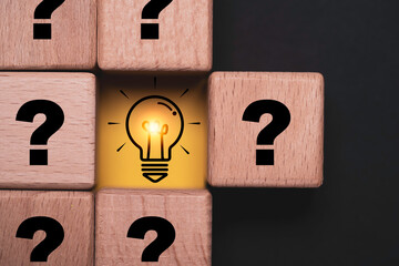 Problem solving concept with a glowing light bulb surrounded by question marks on wooden blocks symbolizing ideas solutions, creativity innovation, critical thinking and decision making. © Dilok