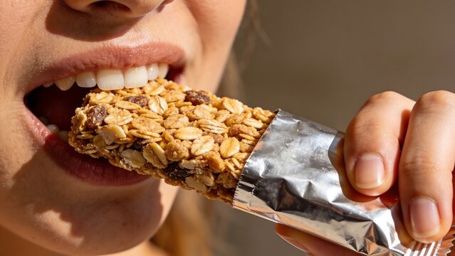 Health-conscious professional eating granola bar snack during busy workday in office setting with clean background