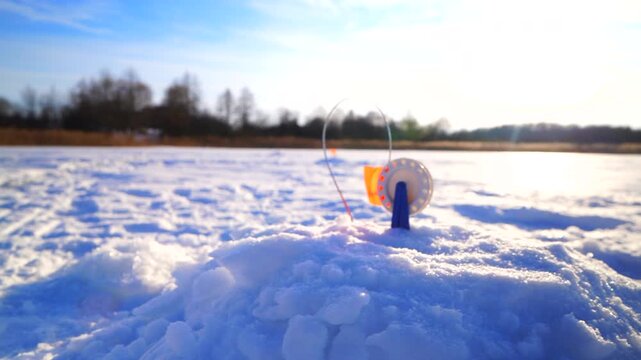 Ice fishing on frozen lake. Zherlitsa gear for winter fishing for predatory fish. Catching fish in a hole in ice on frozen river. Winter fishing. Jigging with Small jigging rod. Winter landscape