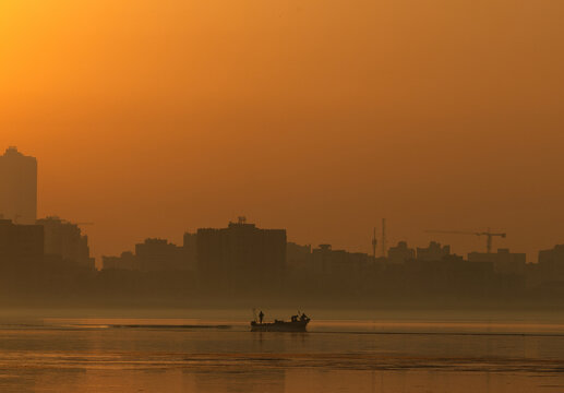 A backlit image of fishermen fishing at Tubli bay during sunrise with highrise building at the backdrop, Bahrain
