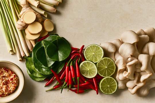 Fresh Thai Tom Yum Ingredients with Lemongrass and Galangal with Lime Leaves and Chilies Arranged on a Pale Stone Surface with Copy Space in Flat Lay