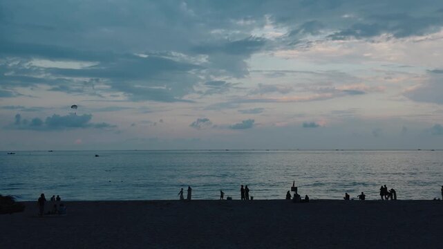 People are relaxing on da nang beach at twilight, enjoying the ocean and a beautiful sky, with a parasailer flying over the water, creating a tranquil scene of leisure and travel in vietnam