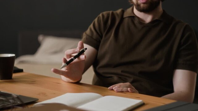 Caucasian young adult man twirling pen at desk near notebook. Visual ideal for marketing campaigns about remote work focus, procrastination, and creative thinking