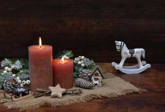 Nostalgic vintage-style Christmas decoration featuring lit candles and a wooden rocking horse against a wooden background with copy space.