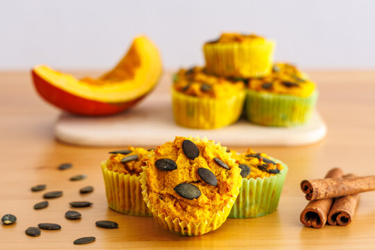 Freshly baked pumpkin muffins decorated with pumpkin seeds, cinnamon sticks and fresh pumpkin slice on wooden table, healthy keto autumn baking concept