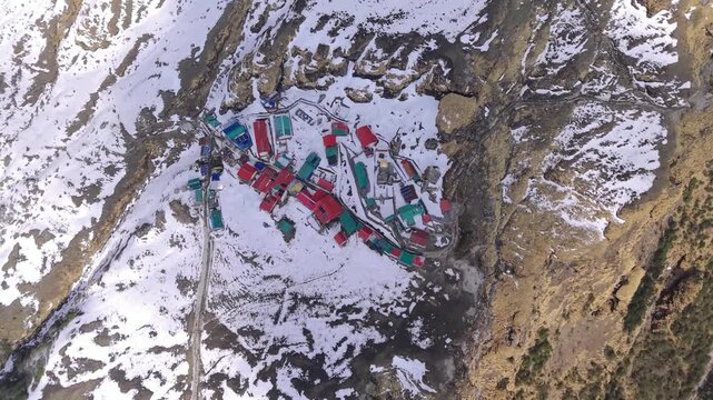Aerial drone view of Tungnath Mahadev Temple in Chopta, Uttarakhand, India, surrounded by snow-covered Himalayan mountains during winter. The footage shows the ancient Shiva temple, nearby local marke