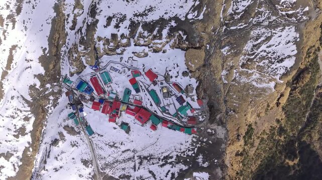 Aerial drone view of Tungnath Mahadev Temple in Chopta, Uttarakhand, India, surrounded by snow-covered Himalayan mountains during winter. The footage shows the ancient Shiva temple, nearby local marke