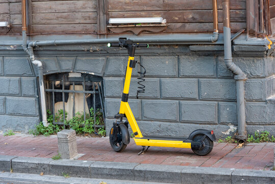 Yellow electric scooter parked on a city street near a building with gray walls