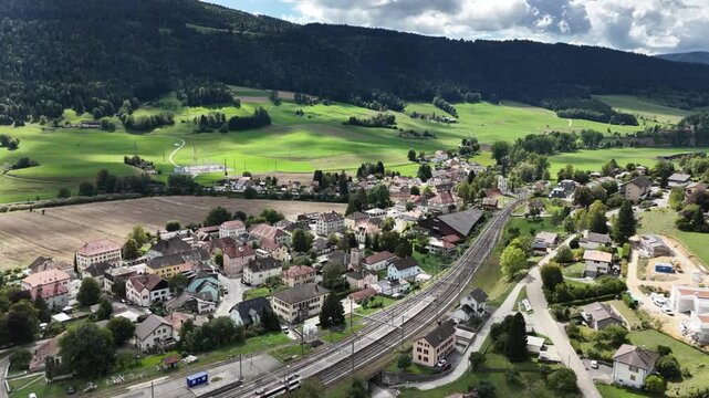 Aerial drone view of Travers, a picturesque village in the Val-de-Travers region of Switzerland. The footage showcases the charming Swiss countryside, traditional buildings, surrounding green landscap