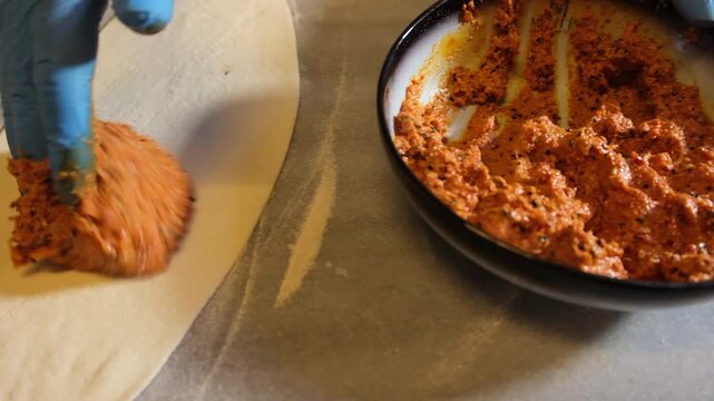 Baker with blue gloves spreading a minced meat mixture on a raw pide dough before baking