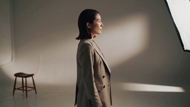 Lifting chin, Asian model in tan blazer adjusting pose as softbox light shifts, posing for portrait