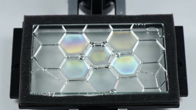 Camera pulling back revealing slide with hex cells and beads on lab, light shifting showing pattern
