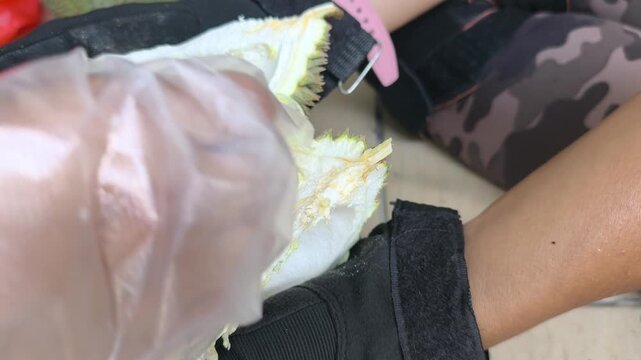 A person demonstrates the proper method to open a fresh durian. Using a sharp machete knife, they skillfully split the spiky husk. The rich yellow fruit pulp is neatly exposed.
