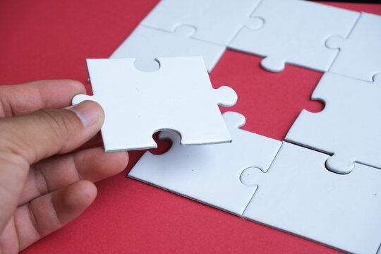 A hand attempts to fit in a missing puzzle piece, symbolizing alliance, unity, teamwork, solutions, success, and problem-solving. It serves as a metaphor for business integration or the challenge of a