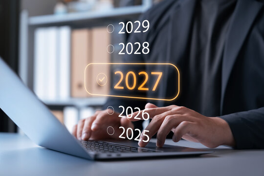 Future business strategy concept. Businessman typing on a laptop keyboard with virtual hologram interface highlighting target year 2027 for corporate planning, digital technology, and success.