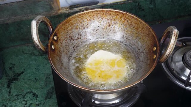 Close up of an Indian woman hand putting the luchi or poori dough on the aluminum pan into hot oil. Cooking puri or luchi on the gas stove at home kitchen.